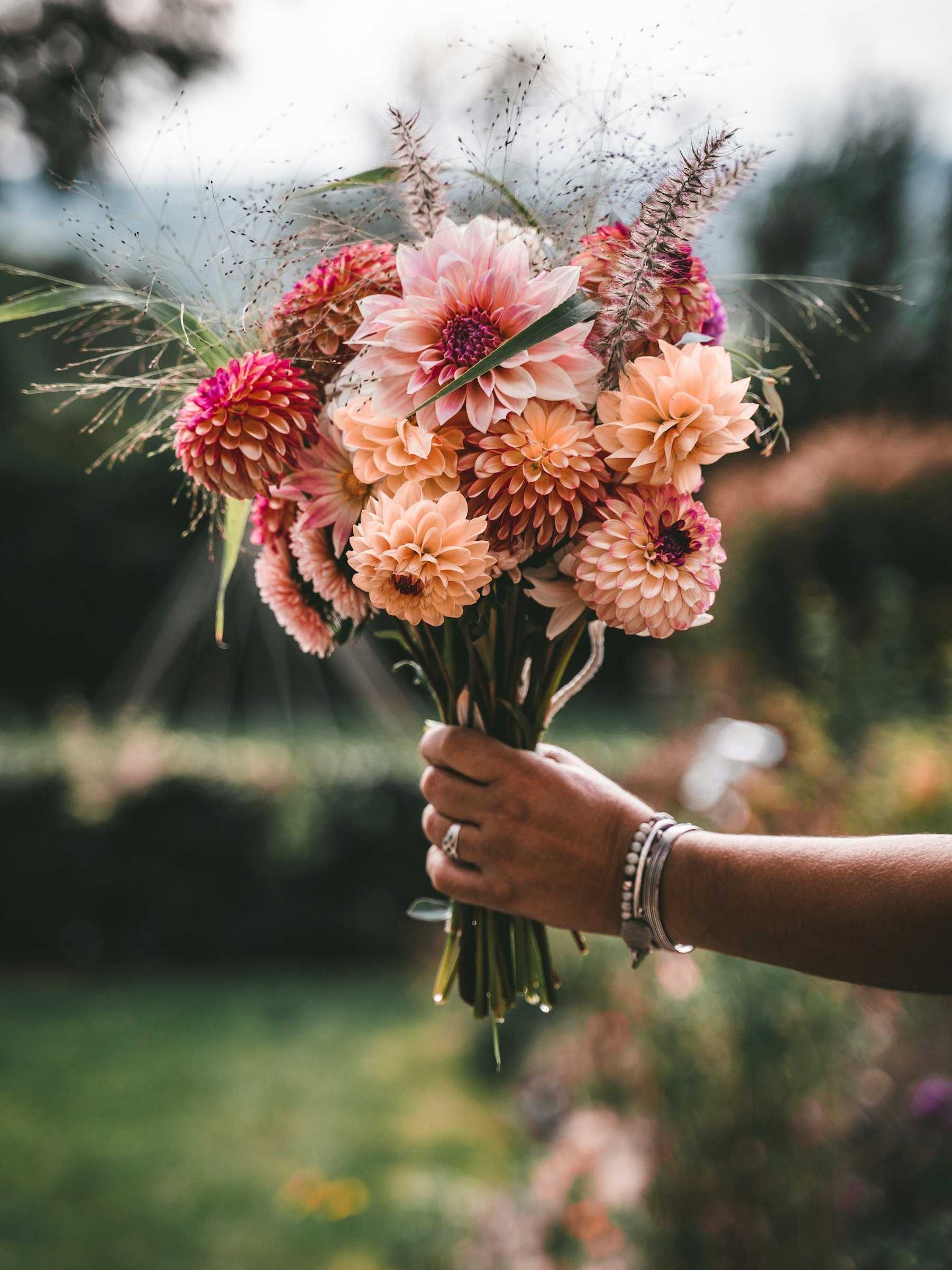 Een hand houdt een handgebonden boeket met perzikkleurige en roze dahlia’s vast.
