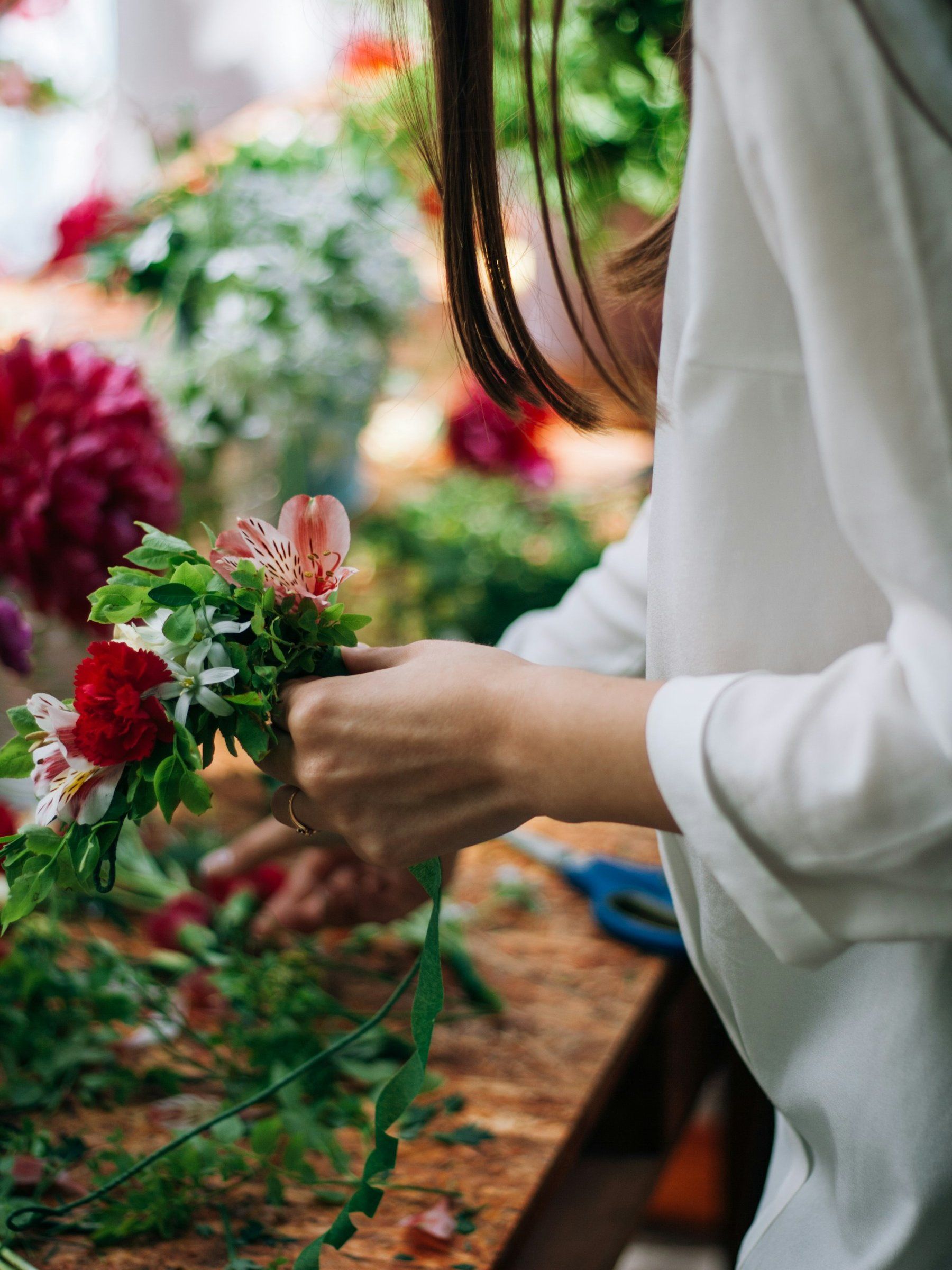 Handen binden rode en witte bloemen op een werktafel vol bloemen.
